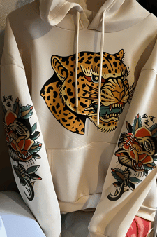 Individueller DTF Transfer auf einem beigen Hoodie: Ein großer Leoparden-Kopf im traditionellen Tattoo-Stil auf der Brust und passende florale Tattoo-Prints auf den Ärmeln – ein Beispiel für hochwertige, vollflächige Textilveredelung.